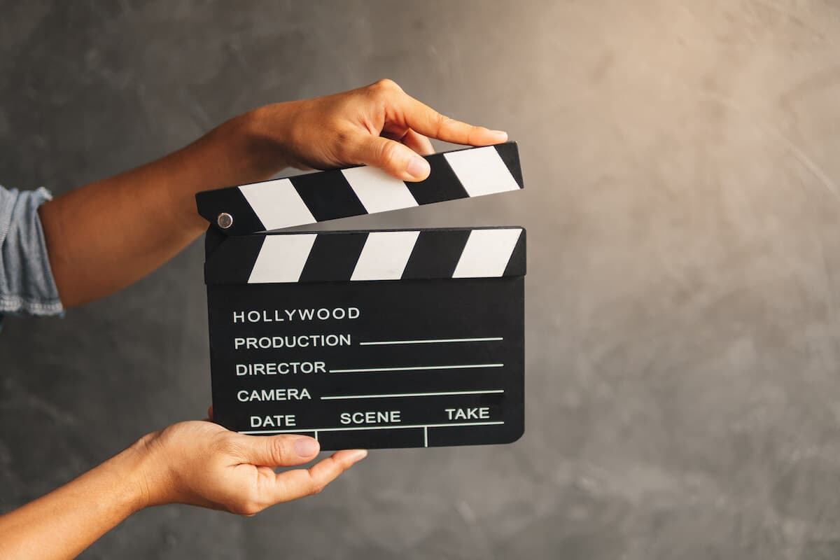Hands holding a film clapperboard, ‘Hollywood Production’ written on it, ready to start a scene.